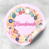 Różowa naklejka z napisem handmade, a na niej klejnoty, diamenty, kryształy.